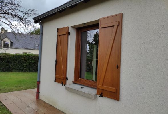 Une fenêtre en bois avec des volets fermés sur un mur clair, entourée d'une pelouse verte.