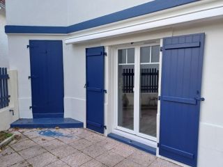 Façade de maison avec des volets bleus et une porte-fenêtre donnant sur une terrasse en pierre.