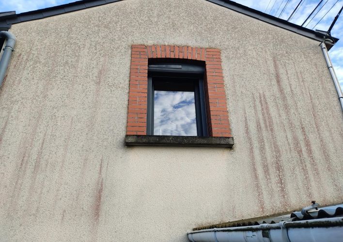 Façade d'une maison avec une fenêtre à encadrement en briques et des traces d'humidité sur le crépi beige.