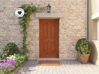 Porte d'entrée en bois massif ornée de plantes grimpantes et entourée d'un jardin fleuri, sur une façade en pierre.