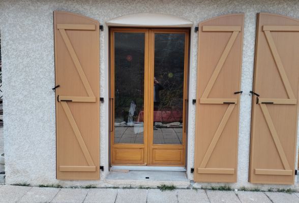 Une porte en bois avec des volets fermés sur une façade en crépi clair.