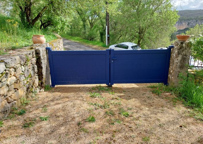 Une porte en bois bleue, entourée de murs en pierres avec des pots de fleurs, donne sur une allée verdoyante sous un ciel