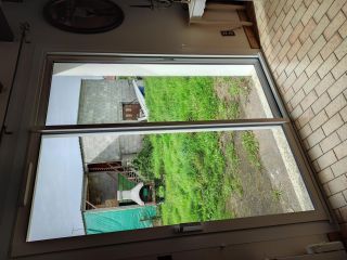 Vue d'une véranda avec baie vitrée donnant sur un jardin en herbe et un abri en béton.