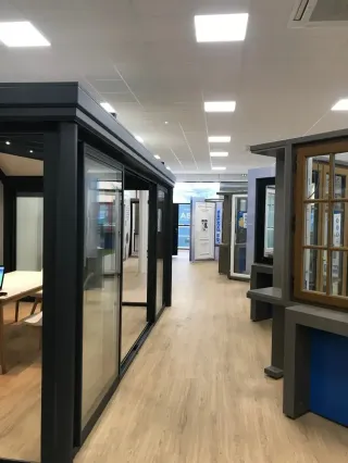 Un showroom moderne avec des présentations de portes et fenêtres sur un sol en bois clair.