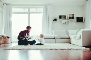 Un père jouant de la guitare pour son enfant dans un salon lumineux et moderne.